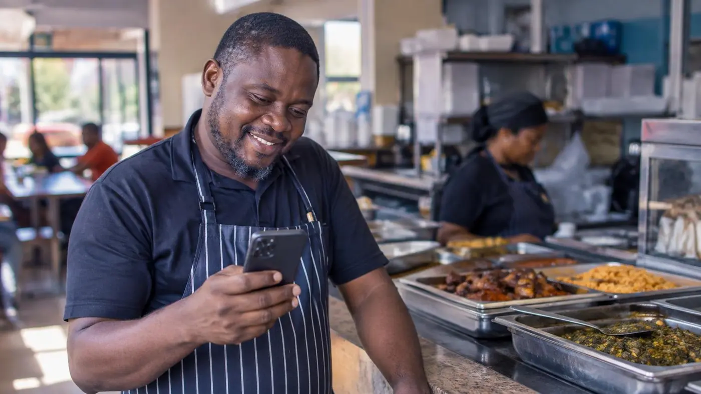 A restaurant owner in Lagos reading a message on his phone at the counter